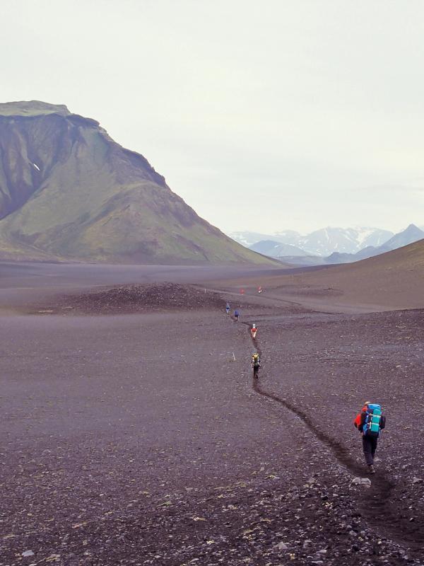 a person with a backpack is walking through a desert with mountains in the background .