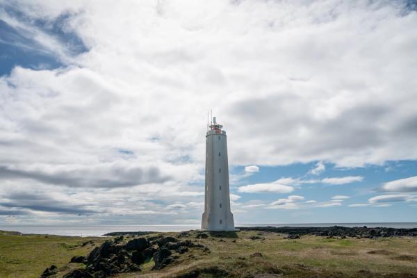 a white lighthouse is sitting on top of a grassy hill next to the ocean .