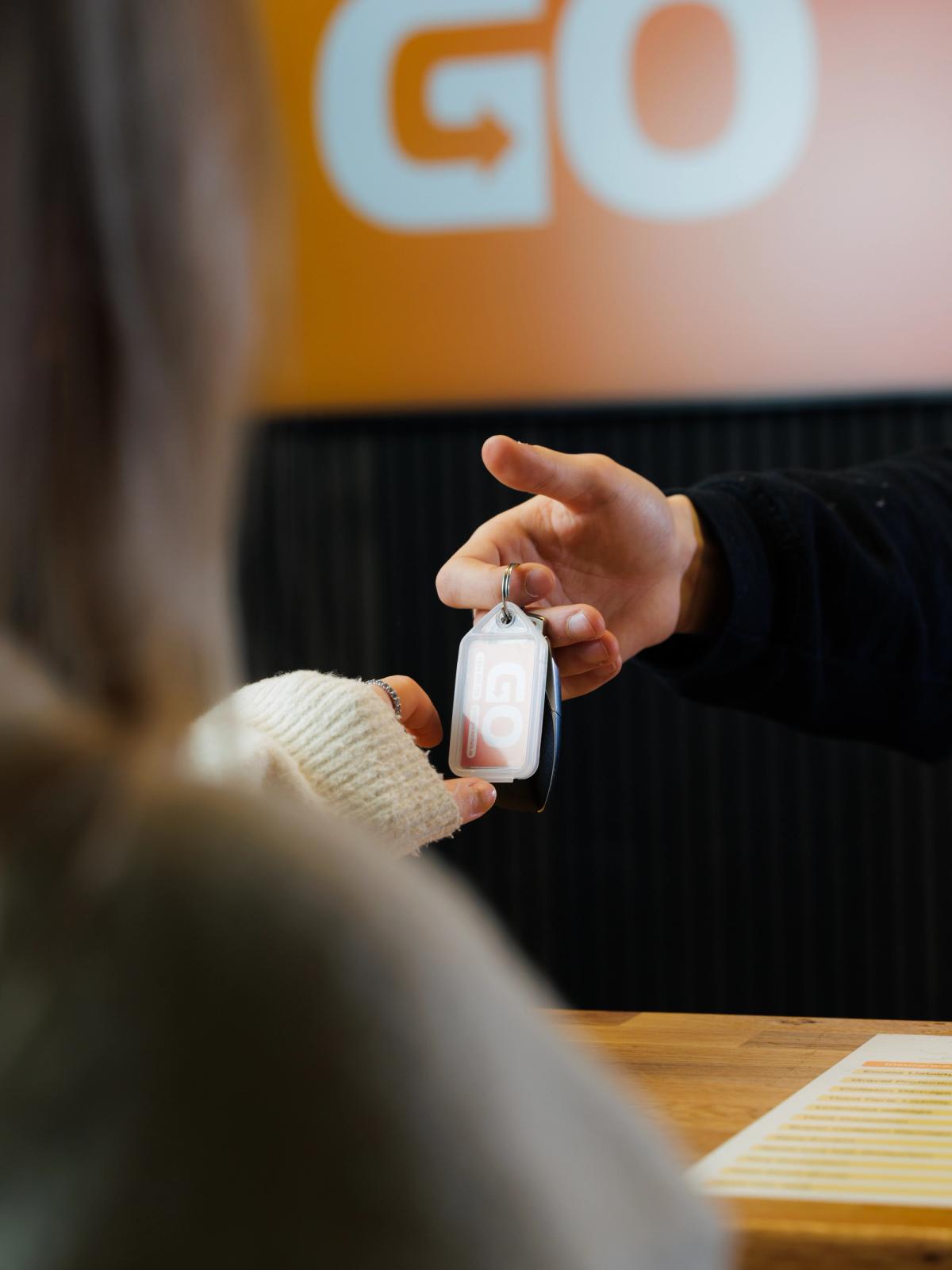 a person handing a car key to another person in front of a sign that says go