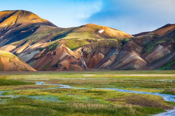Colorful mountains with a waterfall, overlooking a green valley with a winding stream.