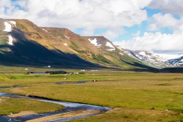 Un río serpenteante atraviesa un valle verde con montañas nevadas y una iglesia roja.