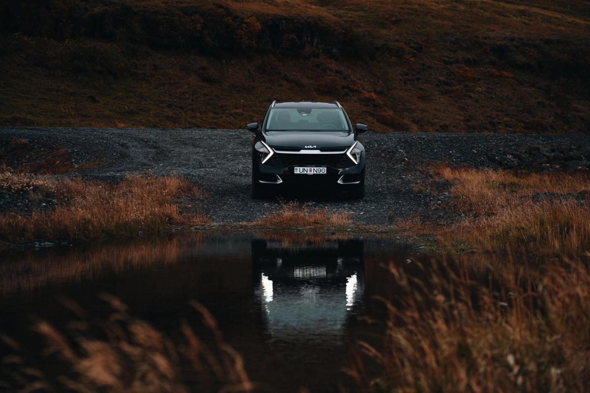 Kia Sportage-jeppi á malarvegi við kyrrt vatn, séður að framan