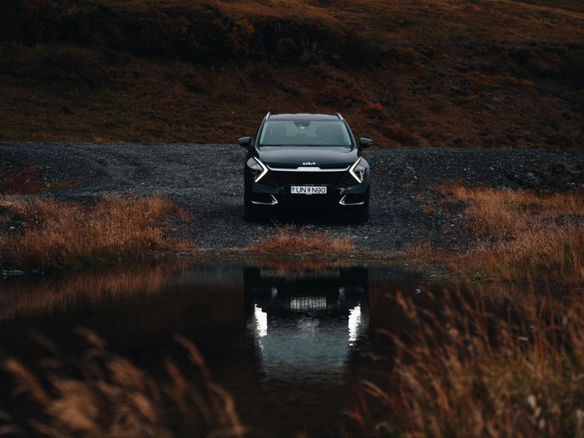 Sportage séð að framan Kia Sportage-jeppi á malarvegi við kyrrt vatn, séður að framan