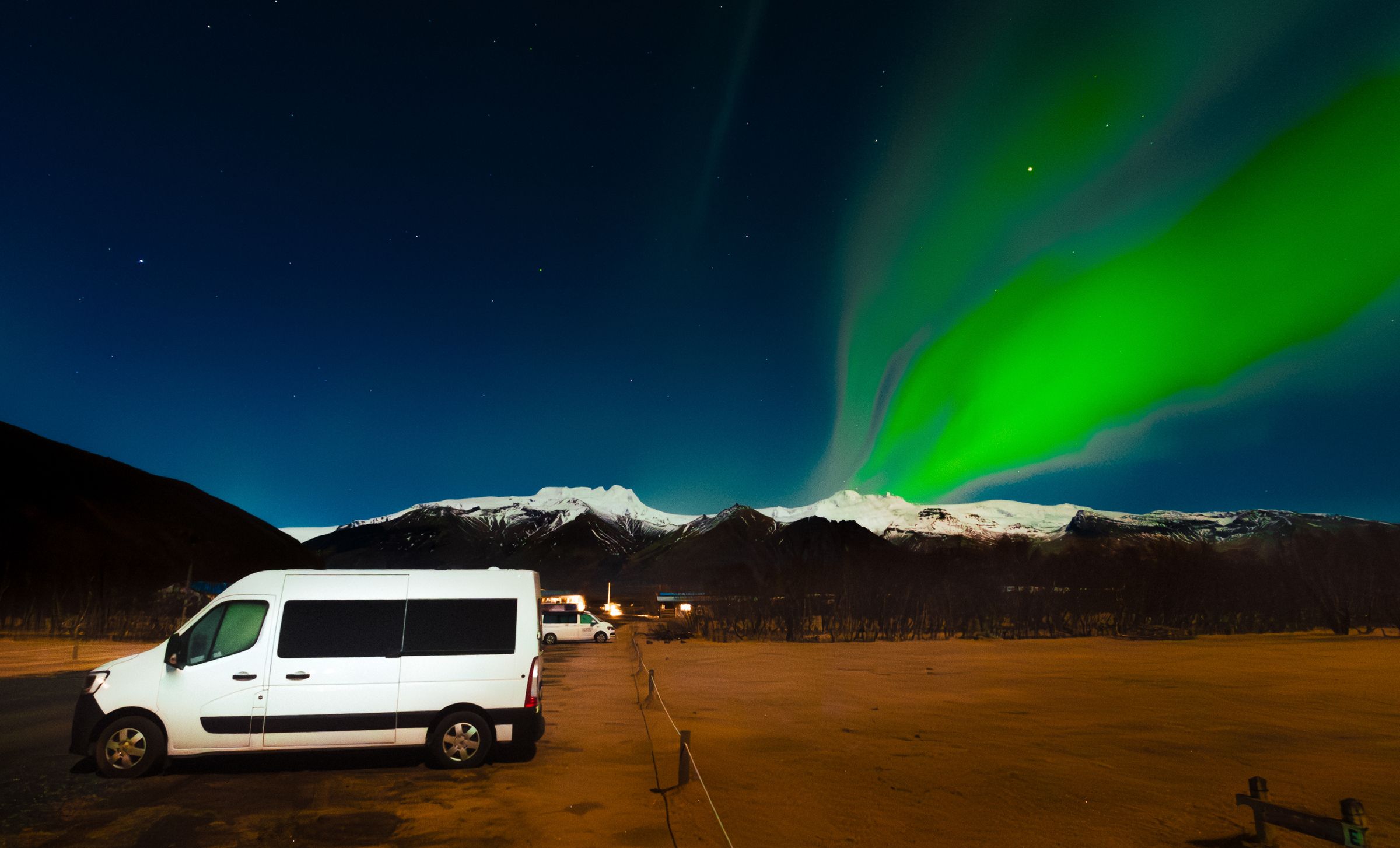 una furgoneta blanca está aparcada en un estacionamiento bajo la aurora boreal.