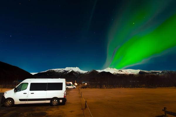 una furgoneta blanca está aparcada en un estacionamiento bajo la aurora boreal.