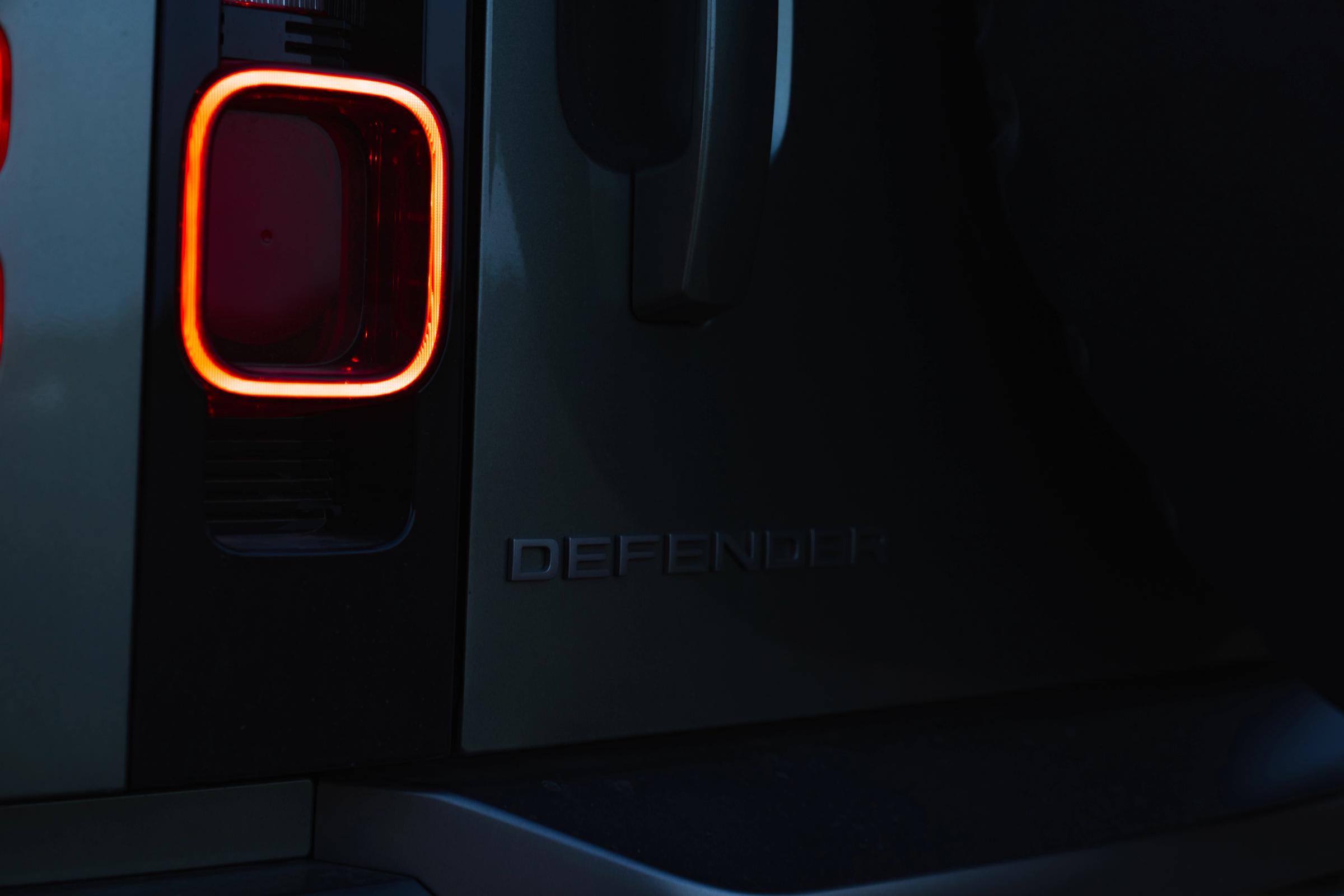 Primer plano de la luz trasera y el emblema iluminados de un Land Rover Defender por la noche, un coche de alquiler de Go Car Rental Iceland