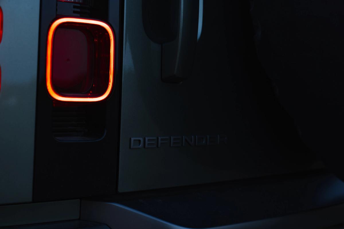 Primer plano de la luz trasera y el emblema iluminados de un Land Rover Defender por la noche, un coche de alquiler de Go Car Rental Iceland