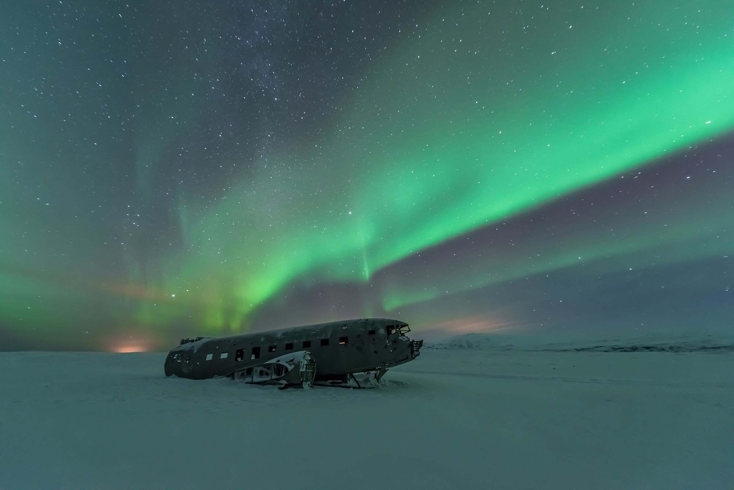 un avión está estacionado en la nieve bajo la aurora boreal.
