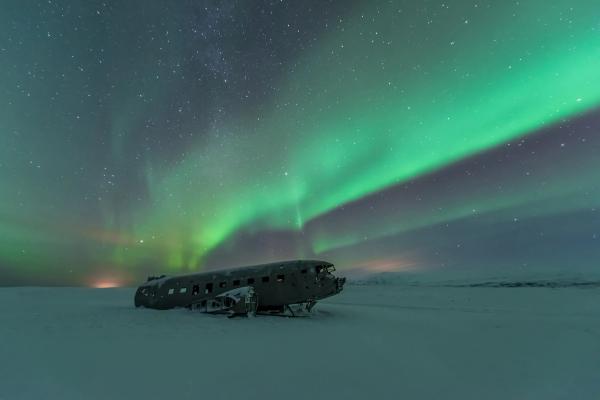 a plane is sitting in the snow under the aurora borealis .