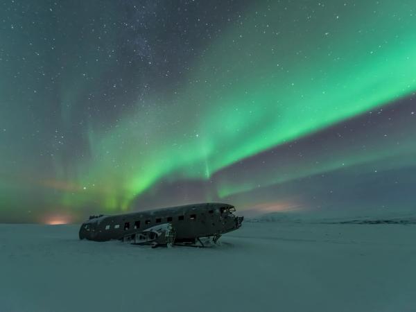 a plane is sitting in the snow under the aurora borealis .