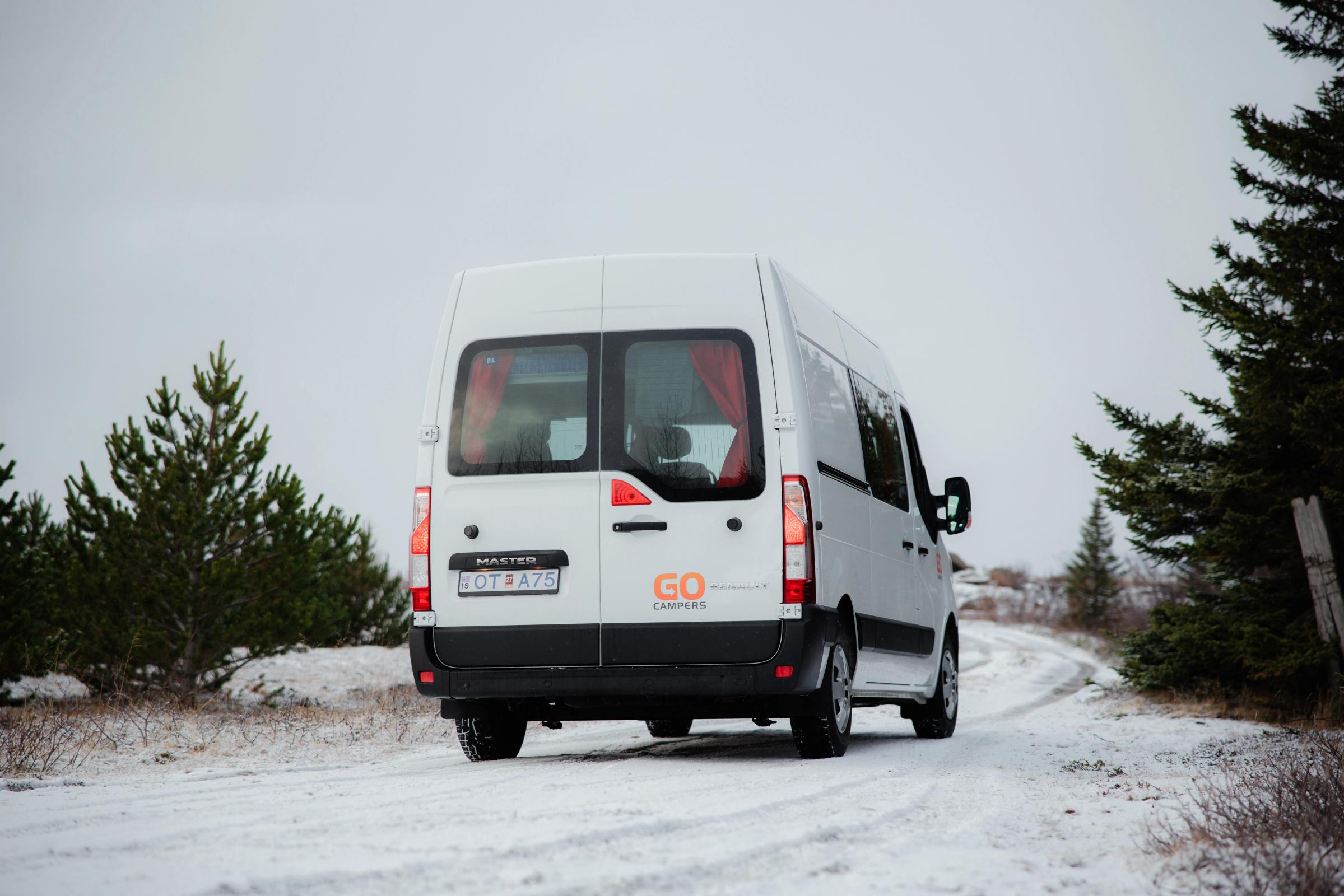 Heckansicht eines großen Wohnmobils auf einem von Kiefern gesäumten Weg, Wohnmobilvermietung Island