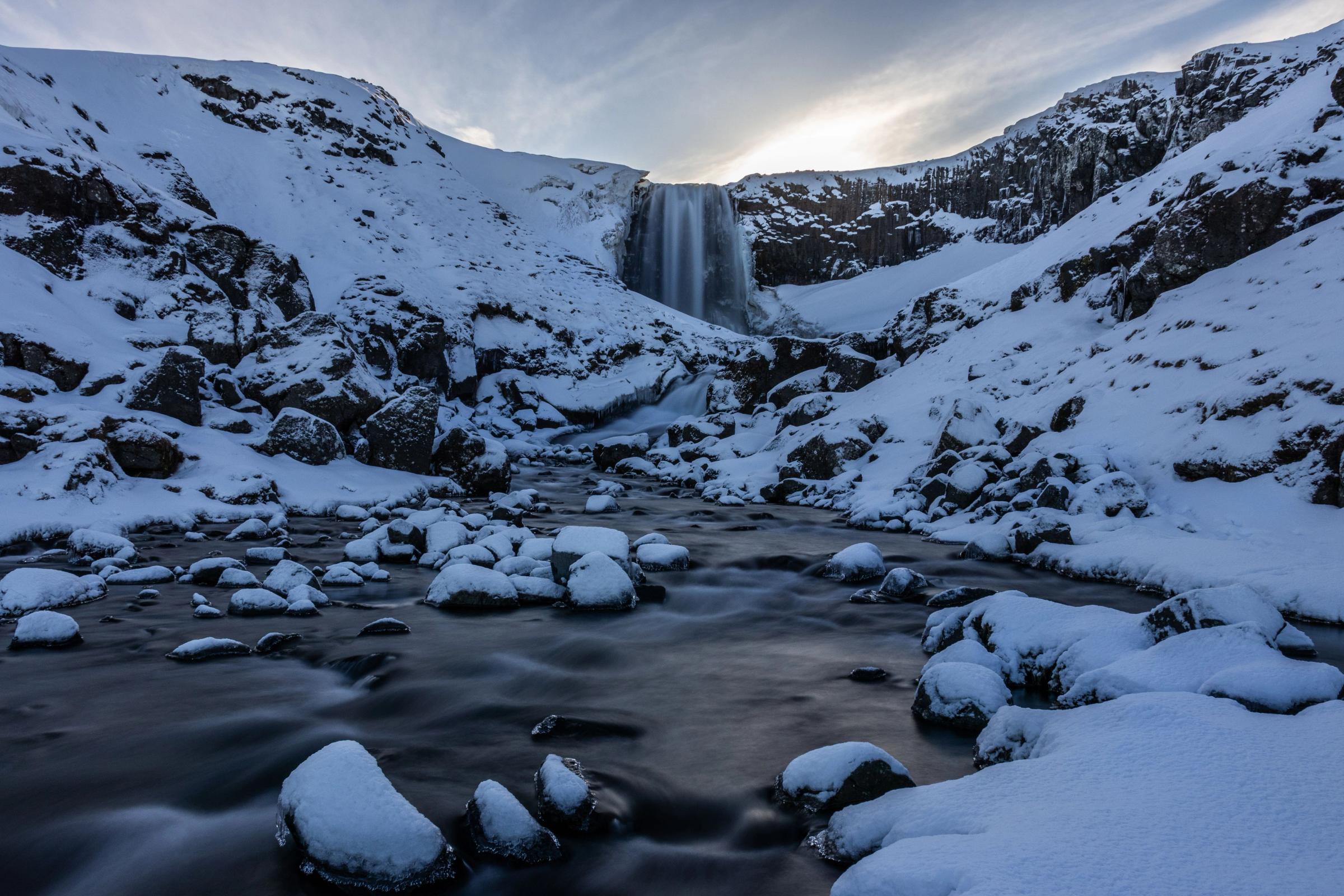a waterfall is surrounded by snow covered rocks and mountains .