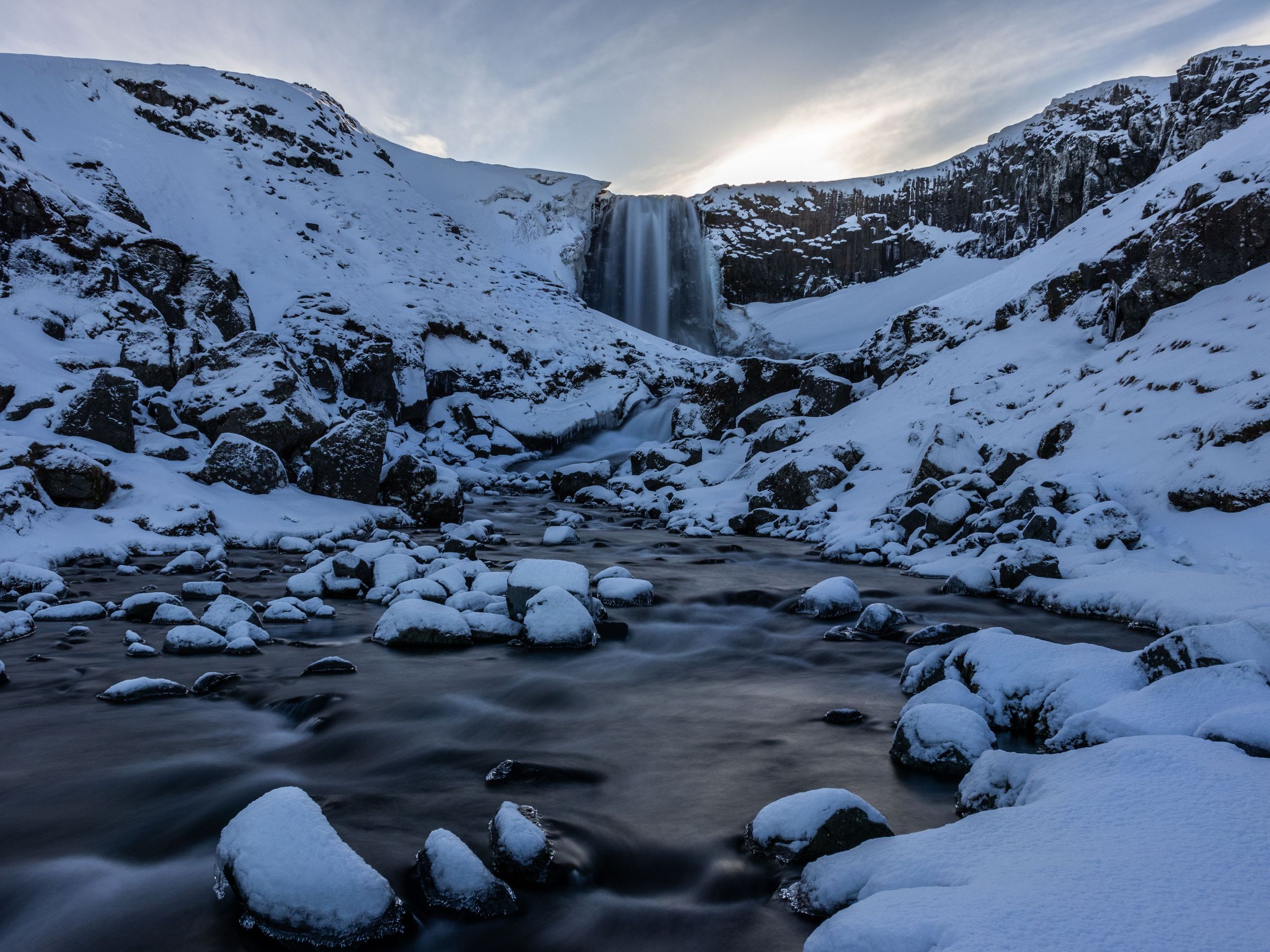 a waterfall is surrounded by snow covered rocks and mountains .