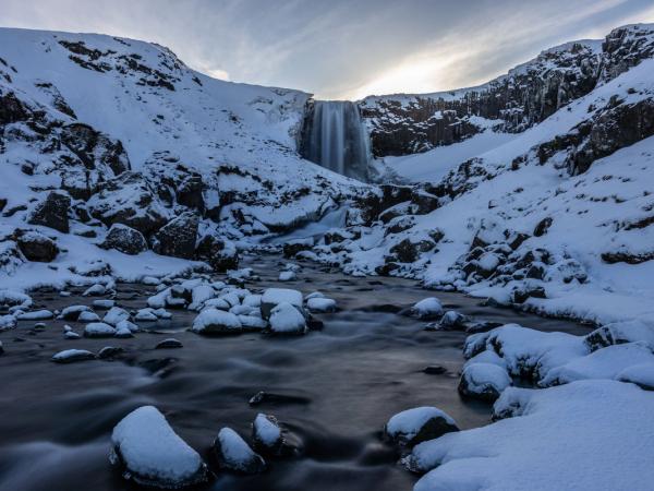 a waterfall is surrounded by snow covered rocks and mountains .