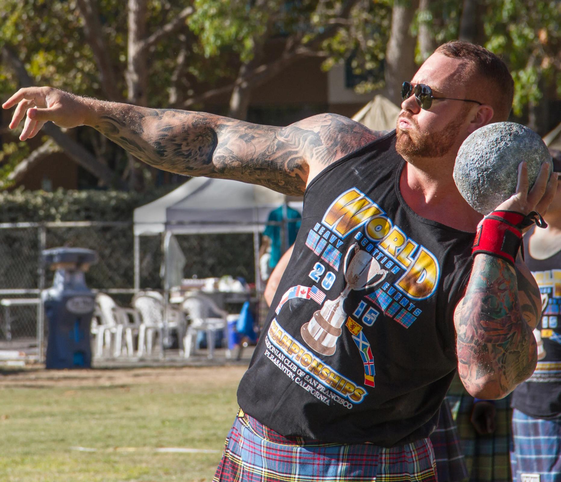 a man in a kilt is throwing a stone .