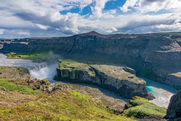 Hafragilsfoss Waterfall in the middle of a canyon with a river running through it .