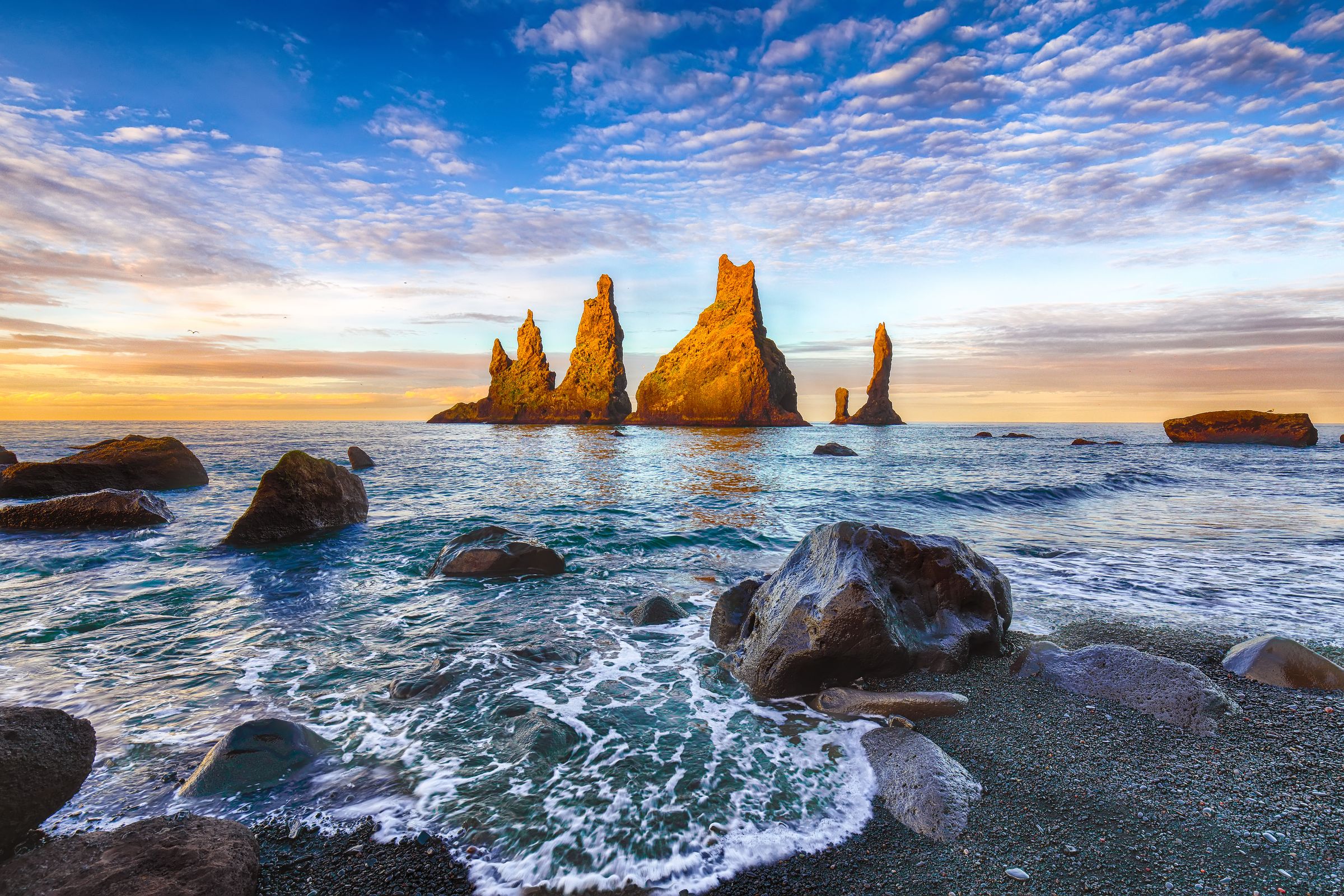 a rock formation in the middle of the ocean at sunset at Reynisfjara, black sand beach in iceland.