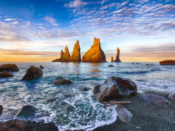 une formation rocheuse au milieu de l'océan au coucher du soleil à Reynisfjara, plage de sable noir en Islande.