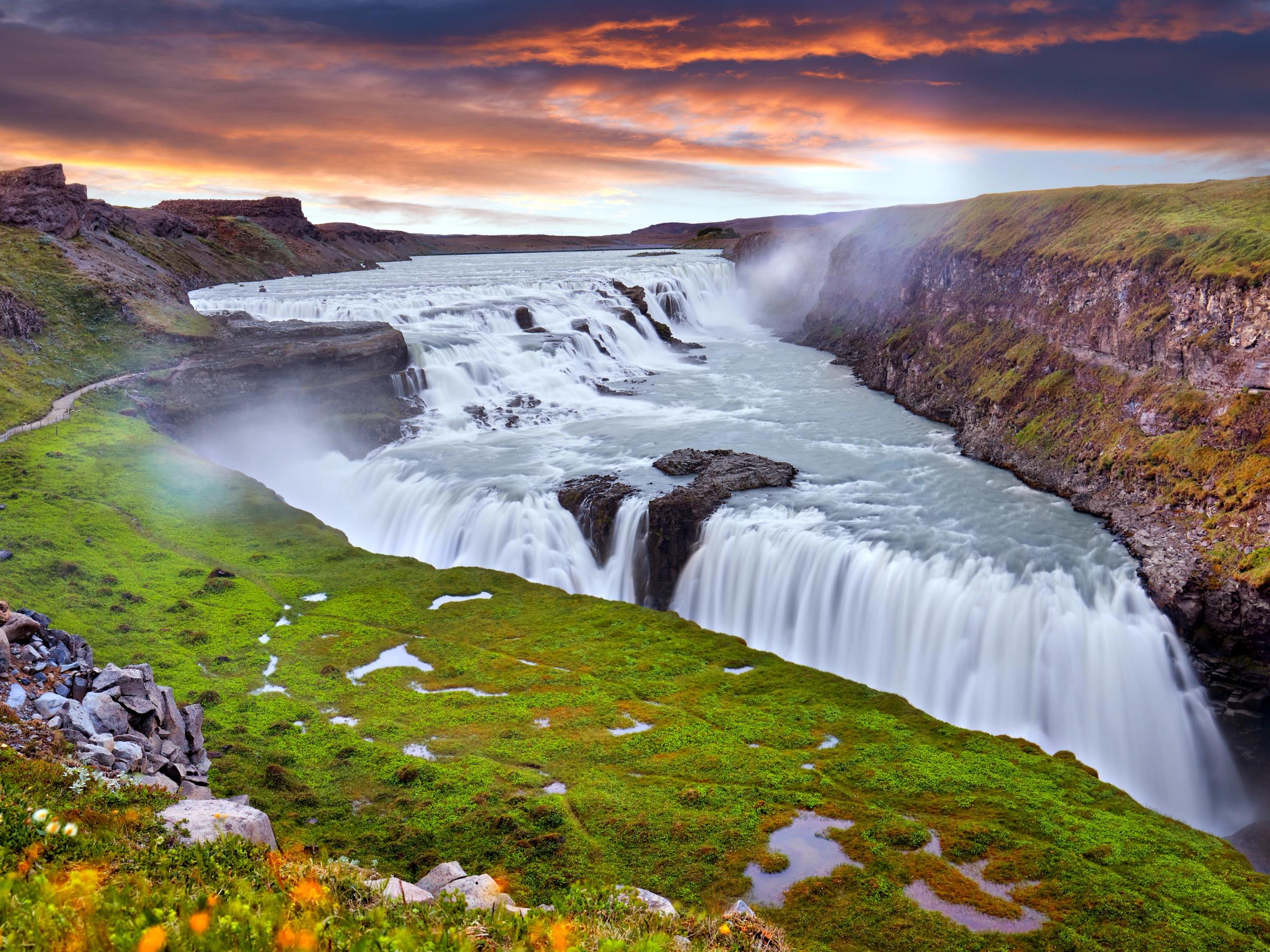 Cascada de varios niveles que cae en un cañón bajo un cielo de atardecer dramático.