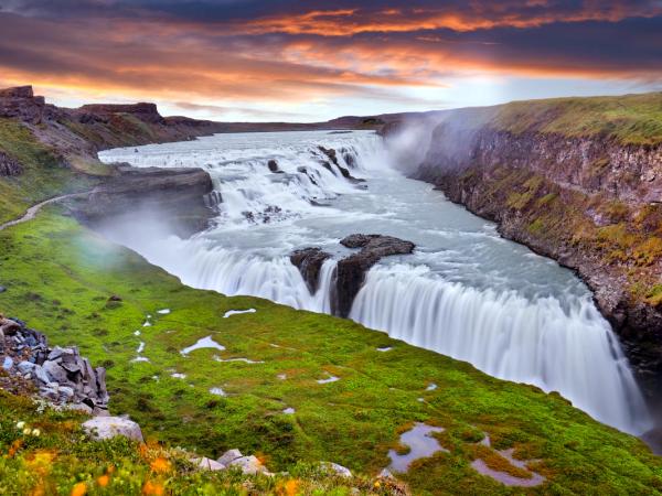 Cascada de varios niveles que cae en un cañón bajo un cielo de atardecer dramático.