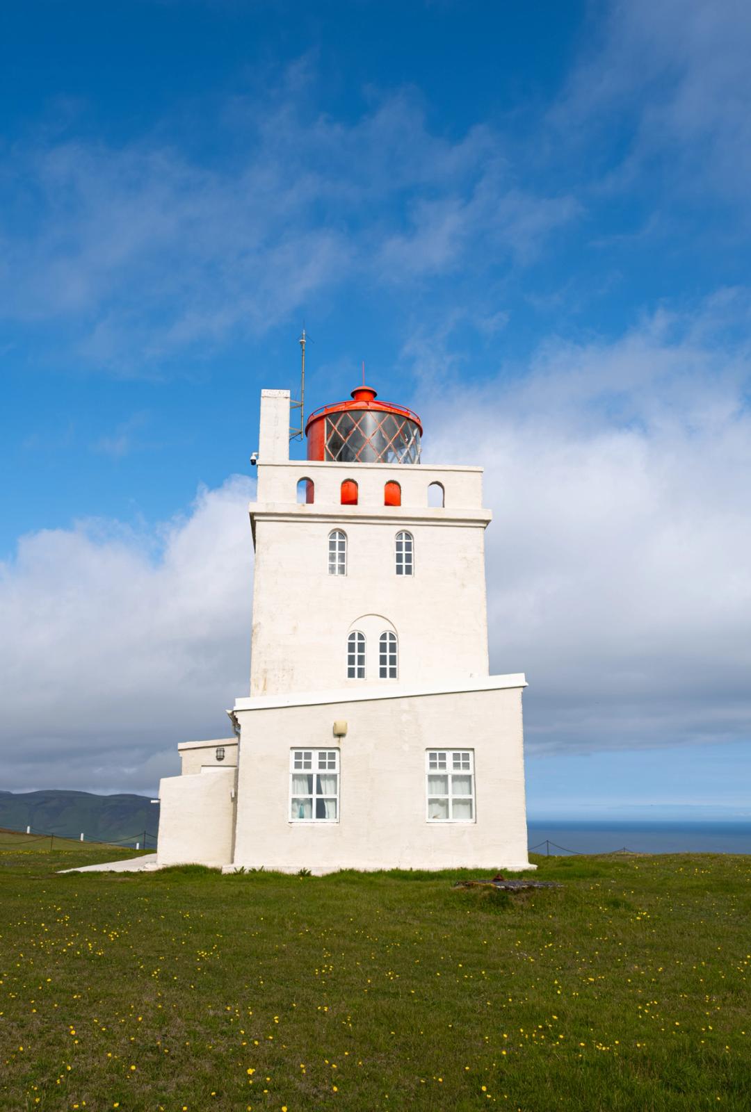 un faro blanco y rectangular con la linterna roja en un día soleado