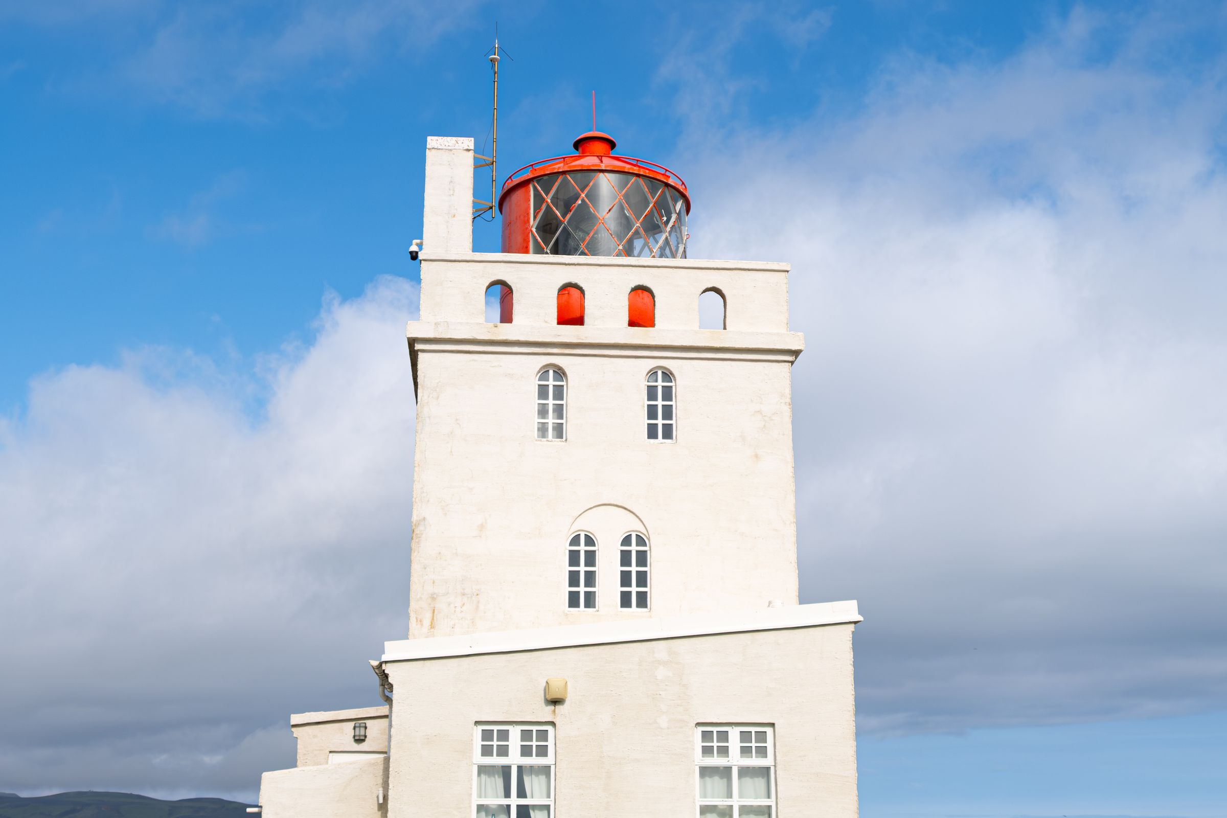 un faro blanco y rectangular con la linterna roja en un día soleado