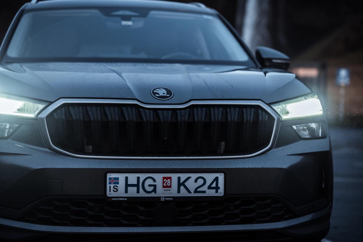 Vista aproximada da grelha dianteira e dos faróis do Skoda Kodiaq, com o emblema da Skoda, ao anoitecer