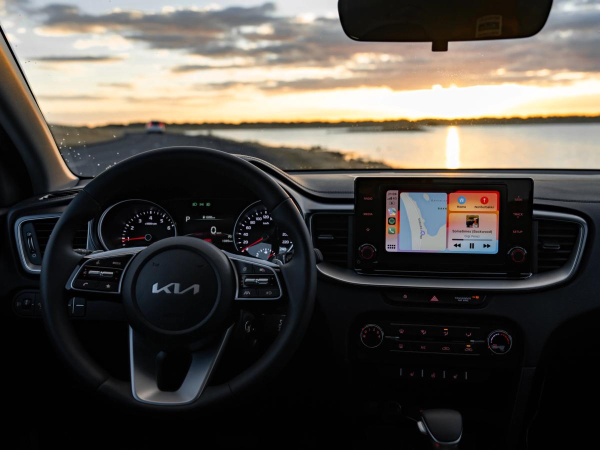 Interior do Ceed ao pôr do sol Vista do interior do Kia Ceed, com volante e ecrã tátil, numa estrada costeira