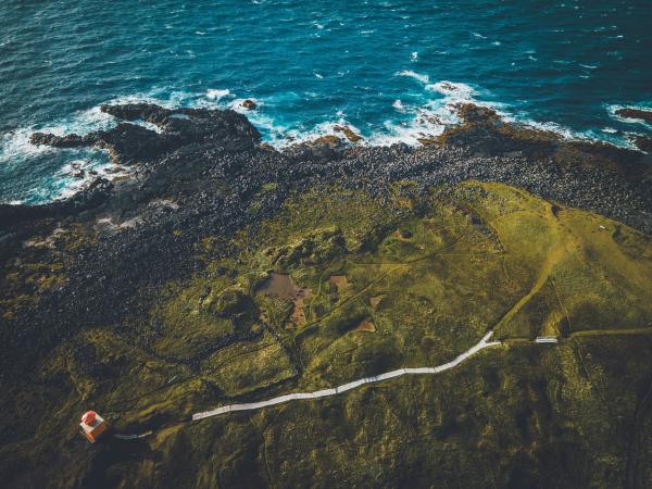 vista aérea de unos acantilados con un camino que lleva hasta un pequeño faro naranja