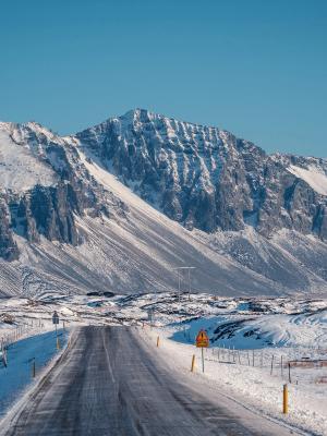 A winter road leads to snow-capped mountains under a clear blue sky.