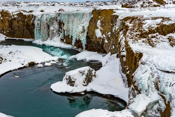 Icy waterfall and blue river in a snowy winter landscape.