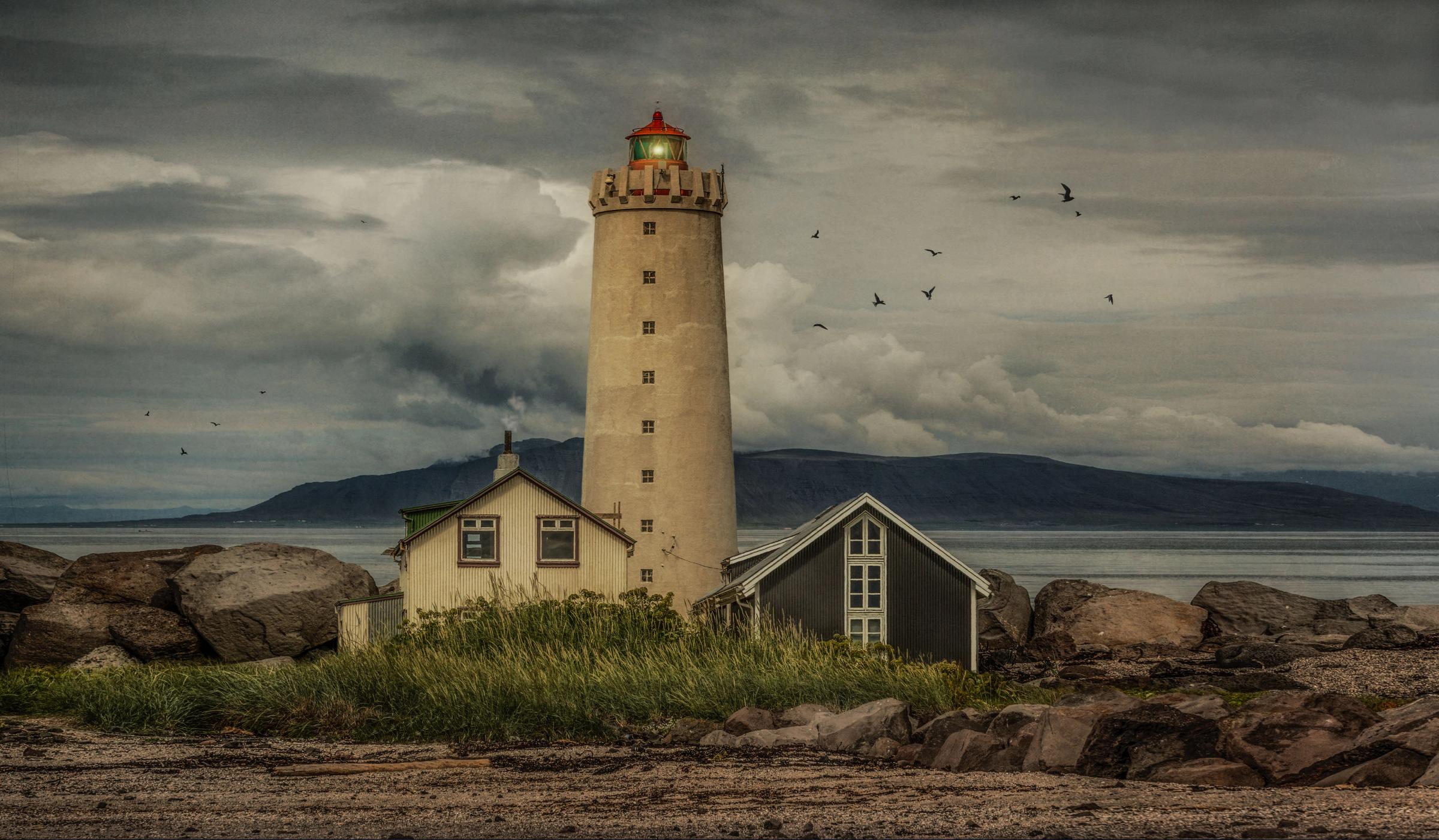 un faro junto a dos casas, una blanca y otra gris oscuro, en un día muy nublado
