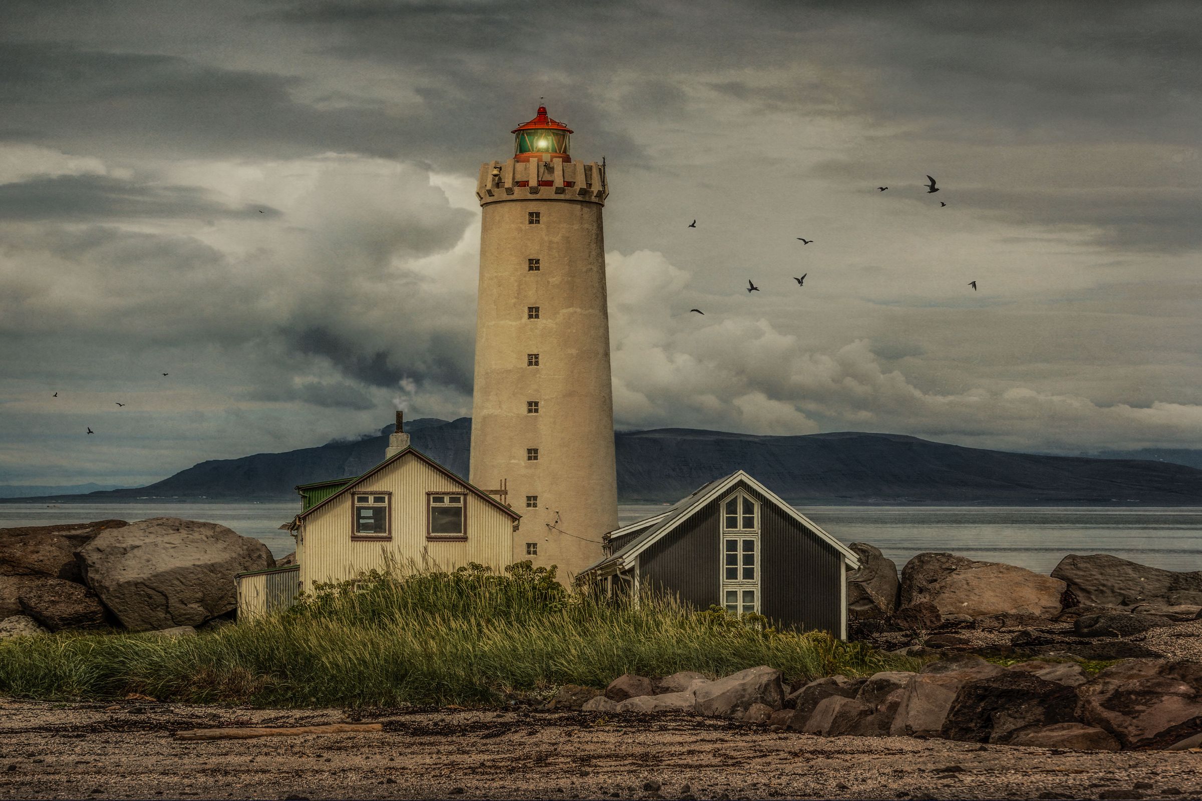 un faro junto a dos casas, una blanca y otra gris oscuro, en un día muy nublado