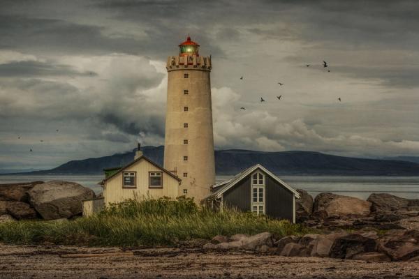 a lighthouse with two houses on a cloudy day