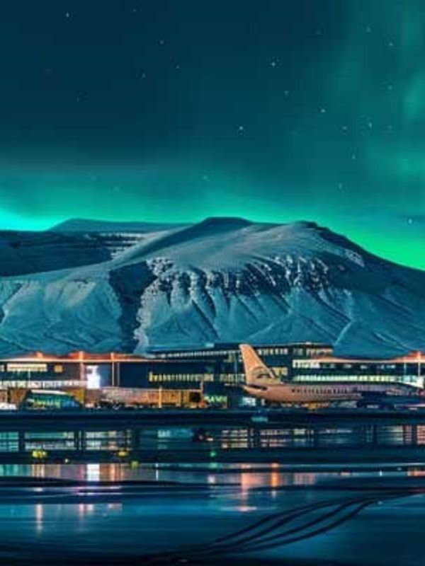 Aeropuerto con montañas nevadas detrás y la aurora boreal en el cielo