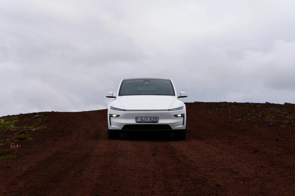 Tesla Model Y visto de frente en una carretera volcánica de tierra roja, alquiler de coches eléctricos en Islandia