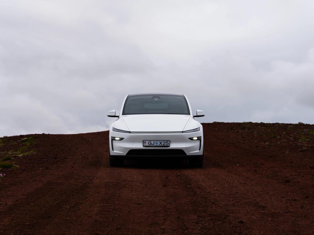 Choque frontal en la cumbre Tesla Model Y visto de frente en una carretera volcánica de tierra roja, alquiler de coches eléctricos en Islandia