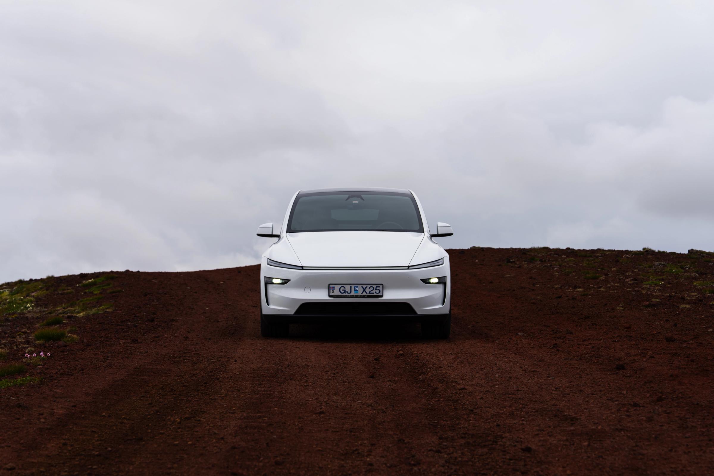 Choque frontal en la cumbre Tesla Model Y visto de frente en una carretera volcánica de tierra roja, alquiler de coches eléctricos en Islandia