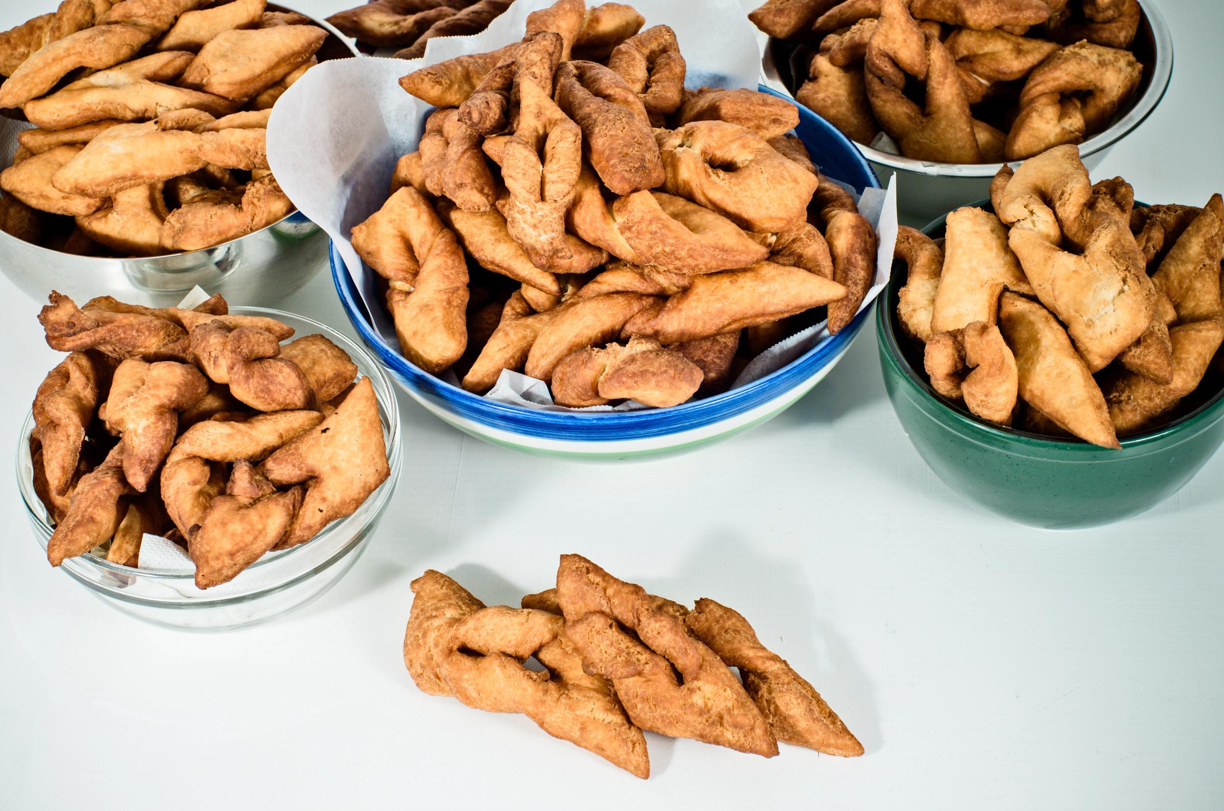 Bowls of golden-brown twisted fried pastries on a white surface.