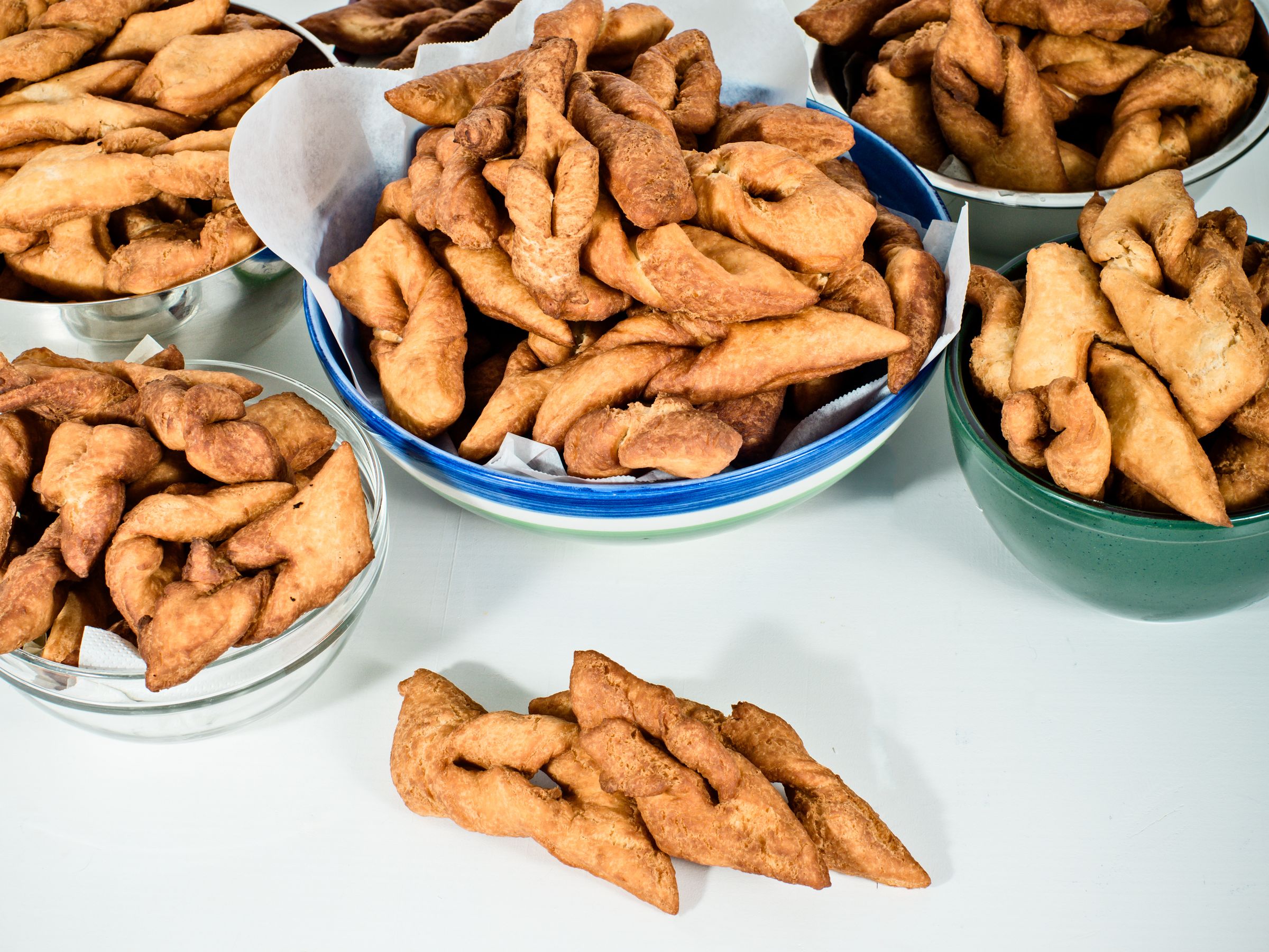 Bowls of golden-brown twisted fried pastries on a white surface.