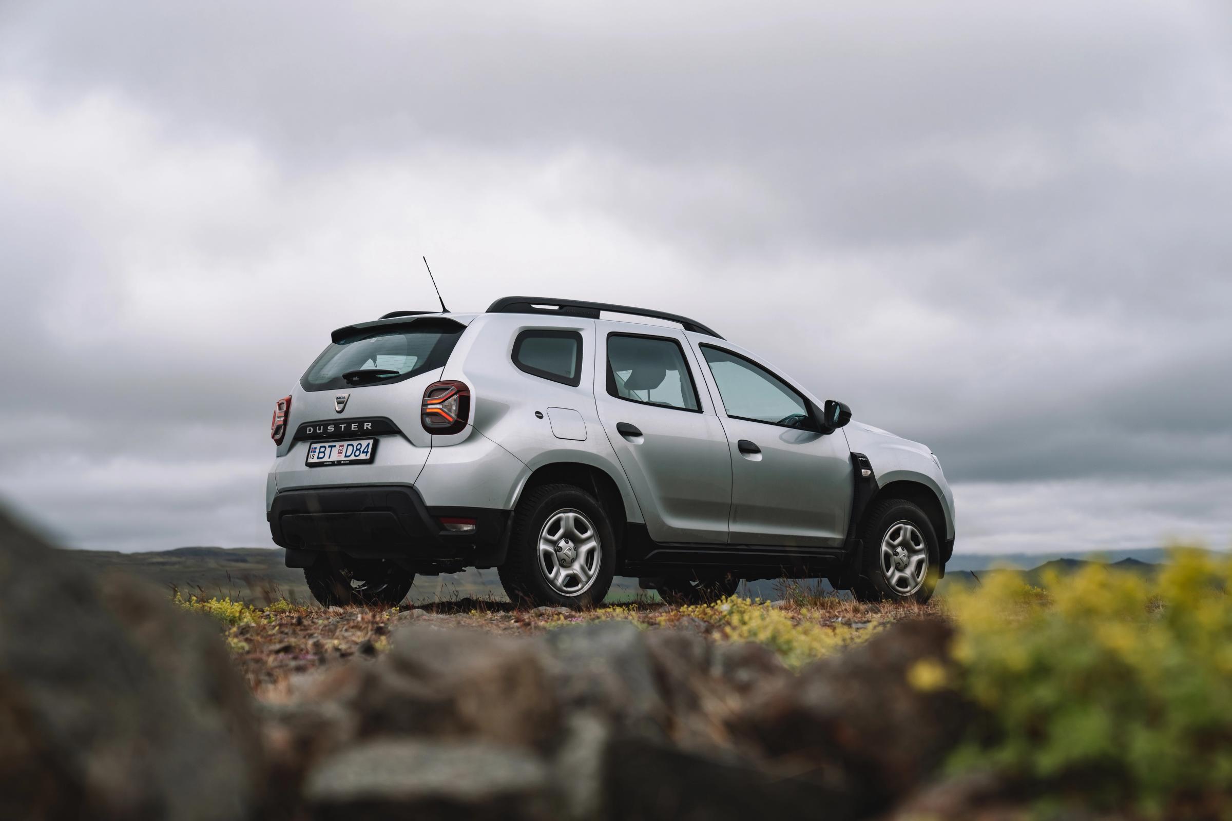 Dacia Duster rear quarter view parked on rocky ground with open landscape and cloudy sky