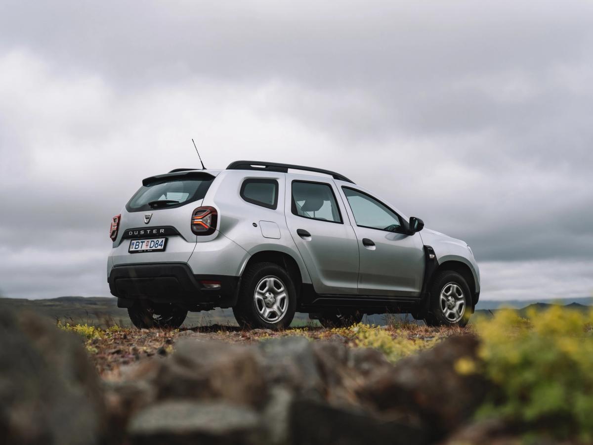 Vista trasera elevada del Dacia Duster Vista trasera de tres cuartos de un Dacia Duster aparcado sobre un terreno rocoso, con un paisaje abierto y un cielo nublado