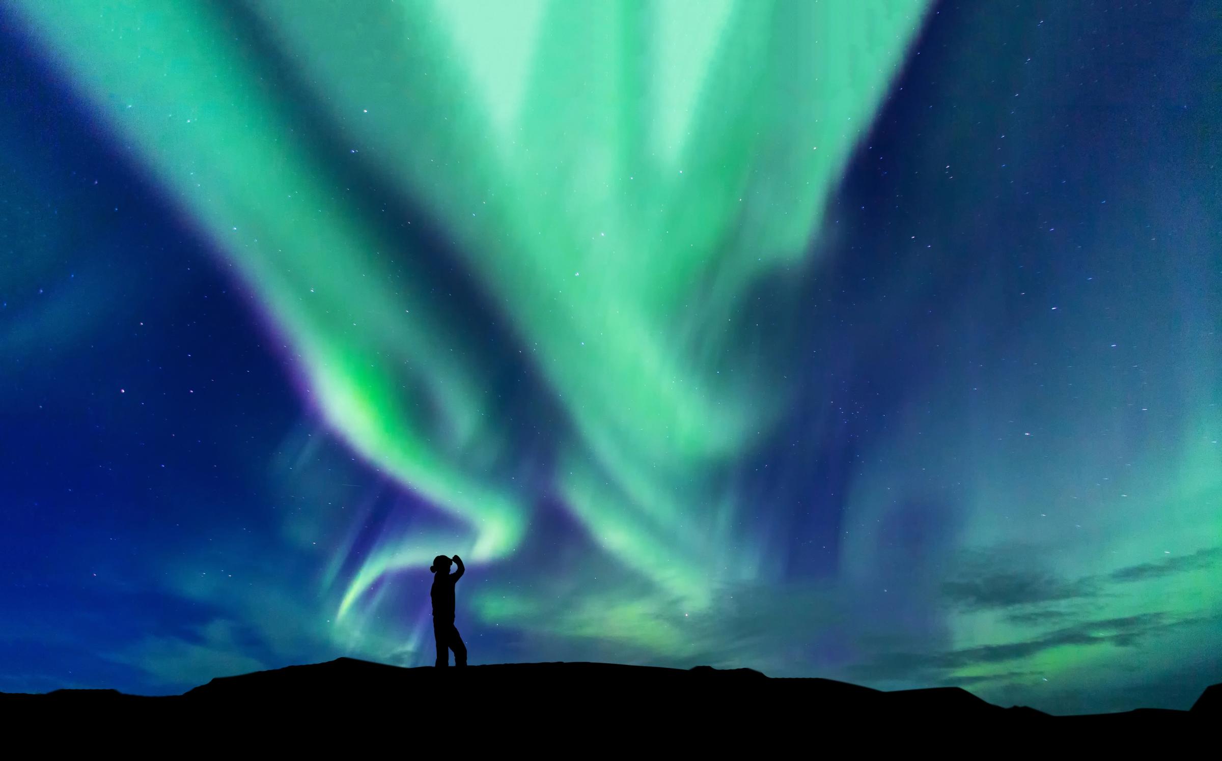 un hombre y una mujer están de pie frente a la aurora boreal.
