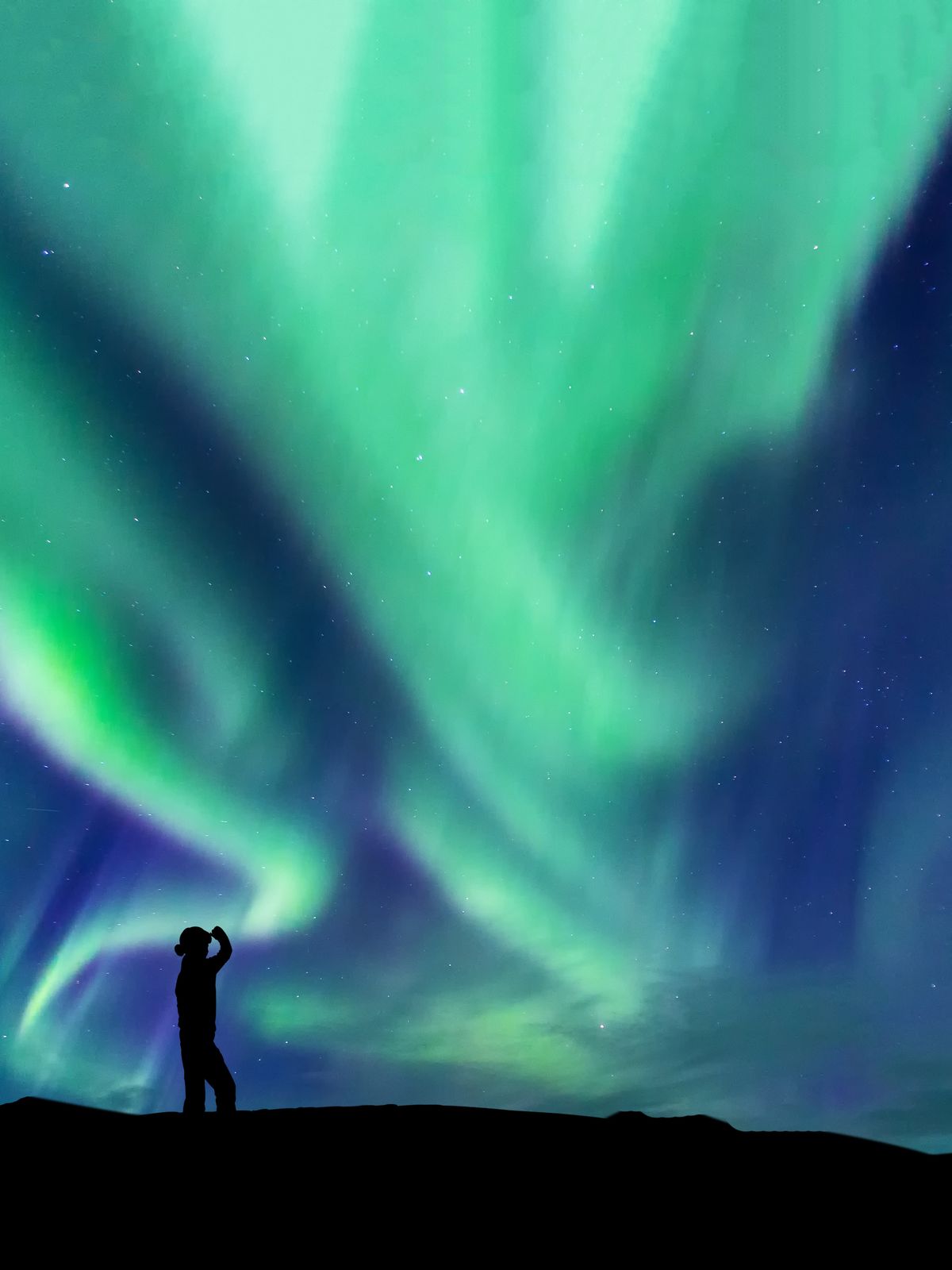 a man and woman are standing in front of the aurora borealis .