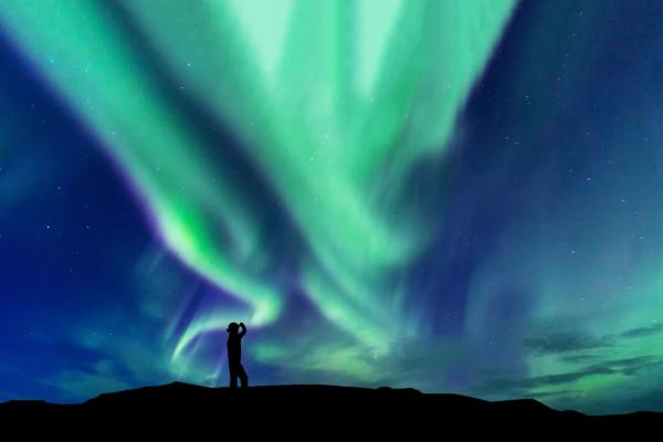 a man and woman are standing in front of the aurora borealis .