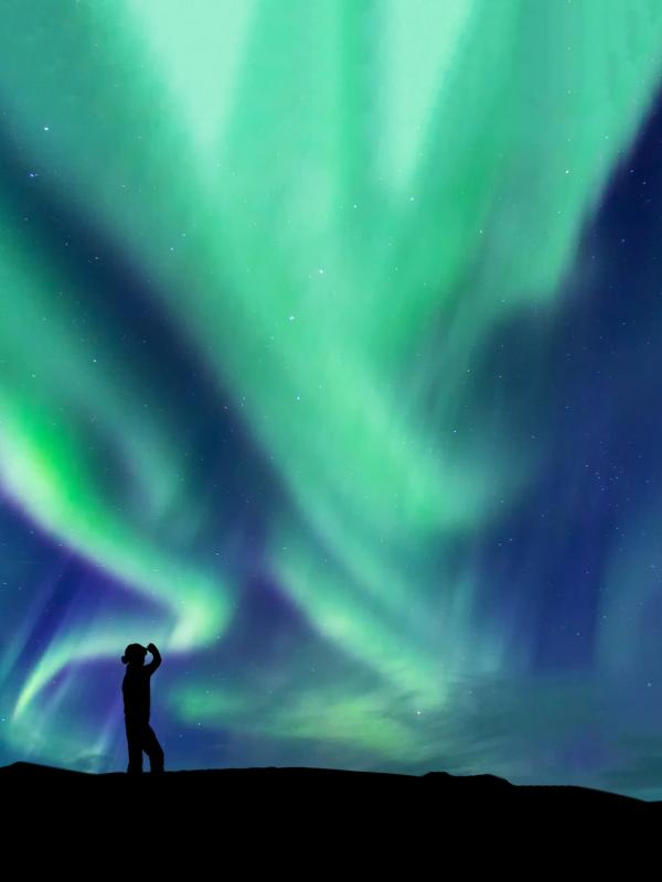 a man and woman are standing in front of the aurora borealis .