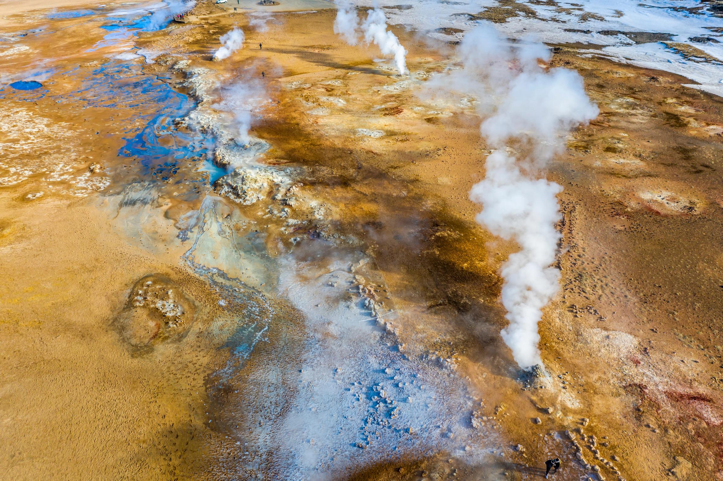 Vista aérea de un paisaje geotérmico con columnas de vapor que se elevan desde un suelo lleno de colores.