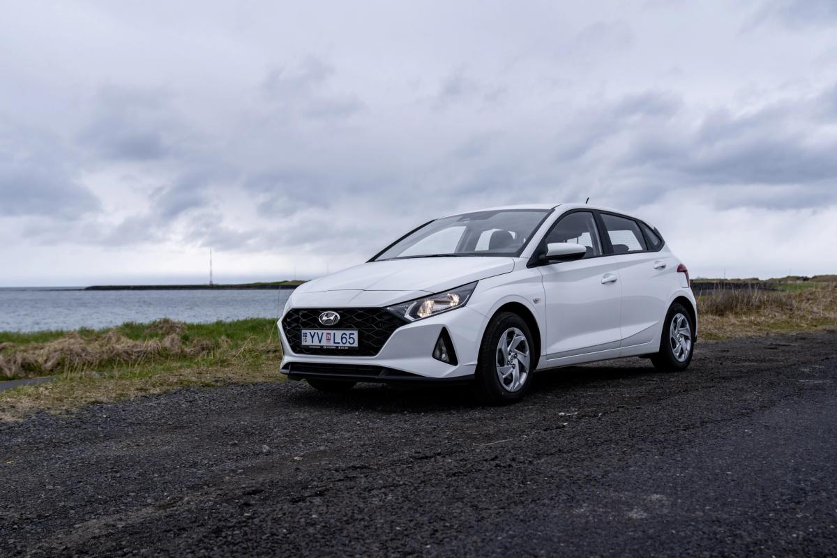 A white Hyundai hatchback parked on a gravel road by the sea under a cloudy sky.