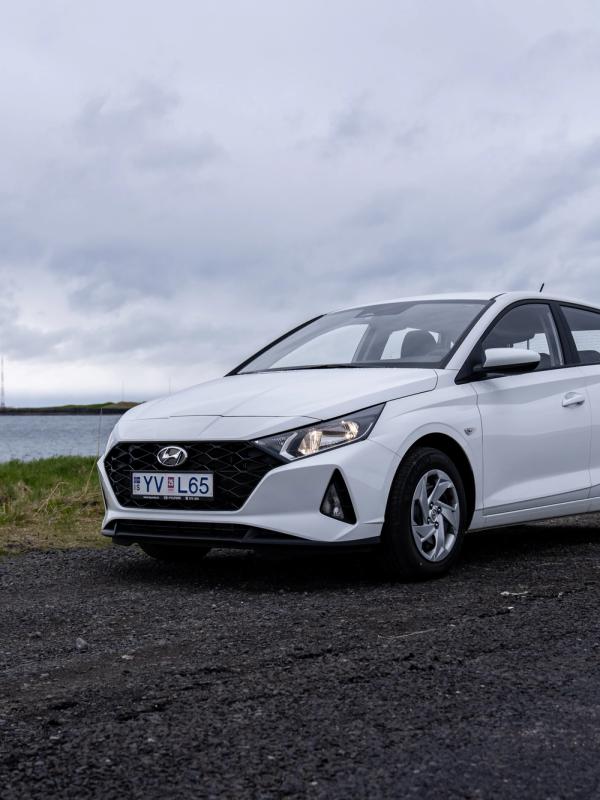 A white Hyundai hatchback parked on a gravel road by the sea under a cloudy sky.
