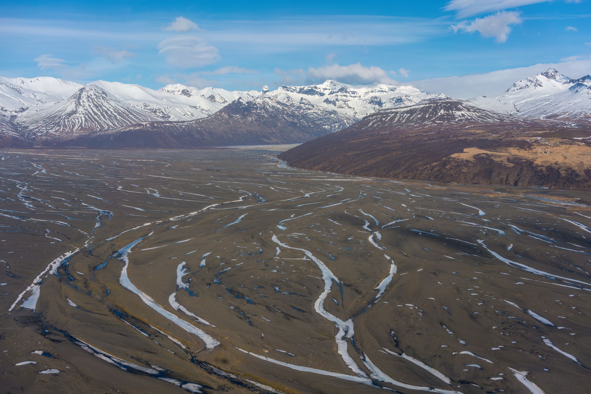 an aerial view of a river flowing through a valley surrounded by snow covered mountains 